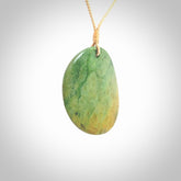 This piece is a large oval round, disc pendant. It was carved for us by Ric Moor from a lovely orange and green piece of New Zealand flower jade. It is suspended on a beige coloured braided cord that is length adjustable.